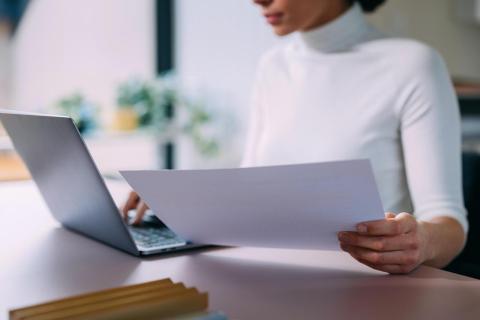 Person at computer holding a stack of paper.